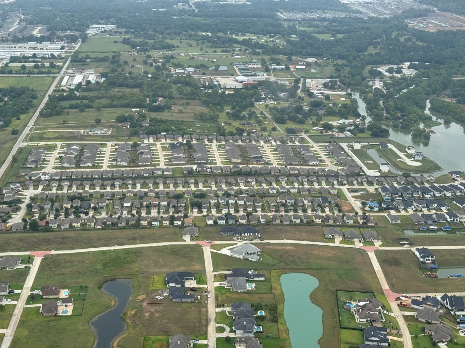 Aerial view of Clearview Estates: streets of single-family homes with larger estate lots and a pond in the foreground, commercial buildings and a river beyond