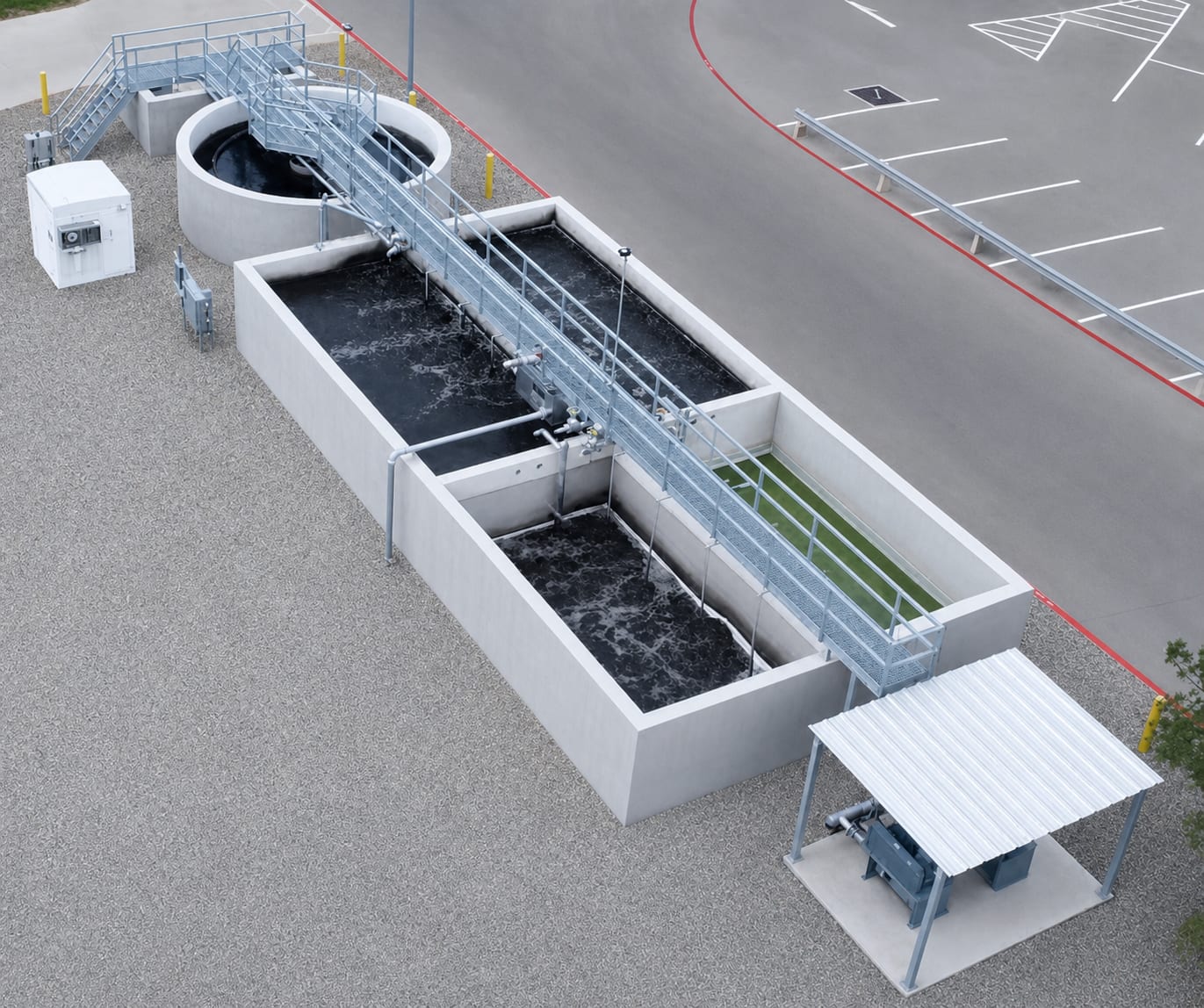 Aerial view of a concrete wastewater treatment plant with two aeration basins, a circular clarifier and a blower set under a canopy